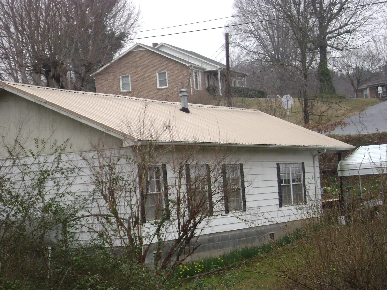 Tan metal roof on a white sided house set into a hillside — Commercial Roofing by Roofing Brothers in Red Rock
